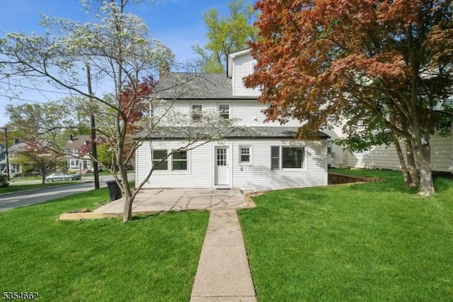 rear view of property with a patio area, roof with shingles, and a yard