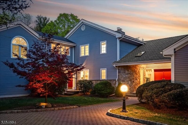 traditional-style home featuring a chimney, stone siding, and roof with shingles