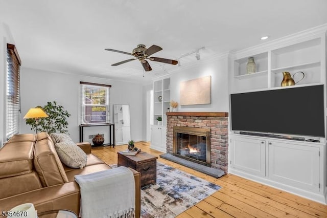 living area featuring a fireplace, rail lighting, built in features, a ceiling fan, and light wood-type flooring