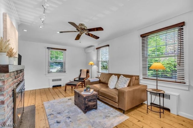 living area with a fireplace, a wall mounted air conditioner, radiator heating unit, hardwood / wood-style flooring, and a ceiling fan