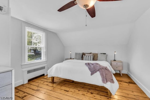 bedroom with light wood finished floors, radiator heating unit, a ceiling fan, a wall unit AC, and vaulted ceiling