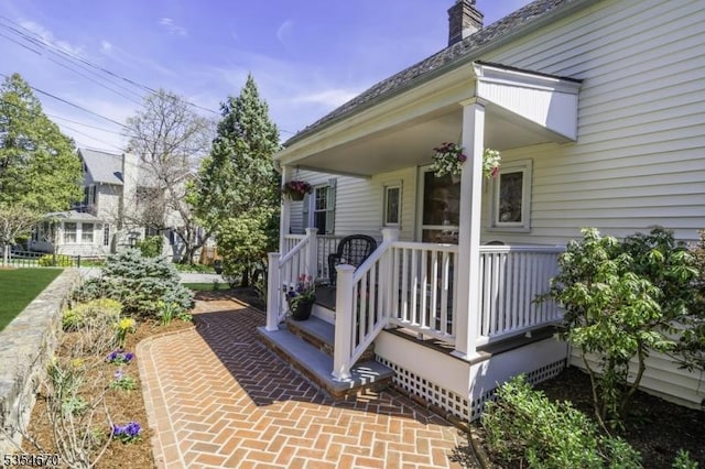 view of exterior entry featuring covered porch and a chimney