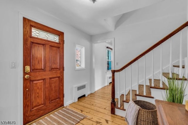 entrance foyer with stairway, radiator, baseboards, and light wood finished floors
