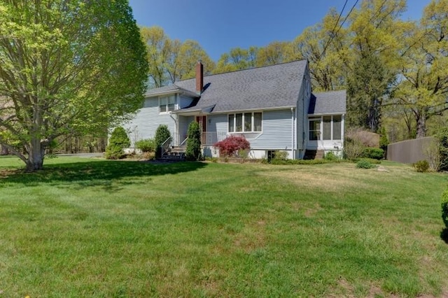 tri-level home featuring roof with shingles, a front yard, a chimney, and a sunroom