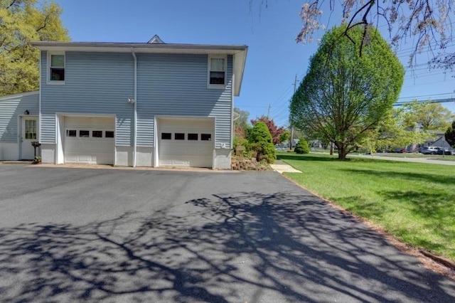 view of property exterior featuring an attached garage, aphalt driveway, and a yard