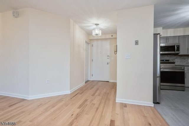kitchen featuring gray cabinets, baseboards, a notable chandelier, stainless steel appliances, and light wood-style flooring