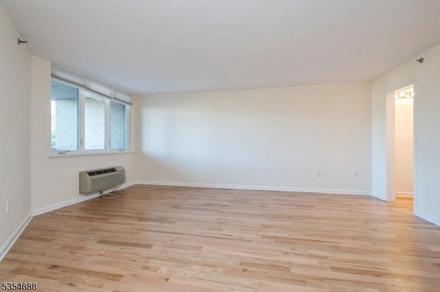 spare room featuring baseboards, light wood-type flooring, and a wall mounted air conditioner