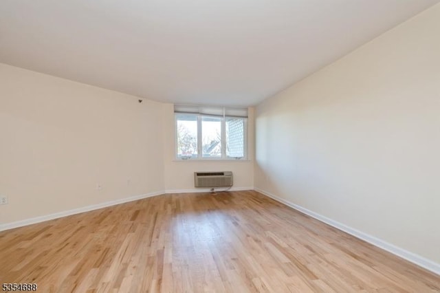 empty room with baseboards, a wall unit AC, and light wood-type flooring
