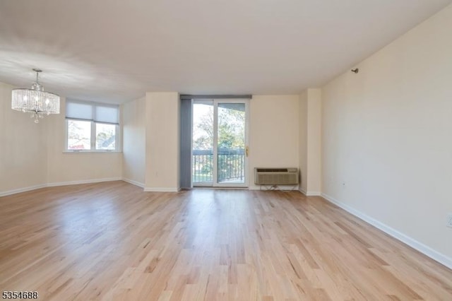 spare room with an inviting chandelier, baseboards, a wall mounted AC, and light wood-type flooring