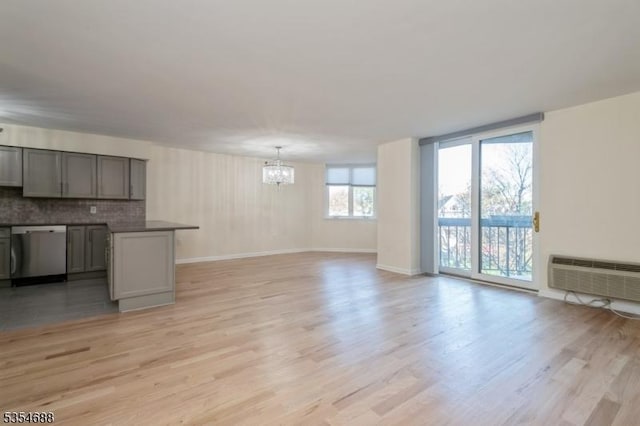 unfurnished living room featuring a notable chandelier, a wall unit AC, and light wood-type flooring