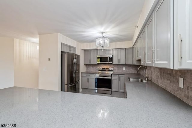 kitchen featuring a sink, appliances with stainless steel finishes, decorative backsplash, and a notable chandelier