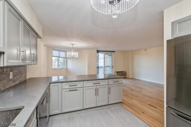 kitchen with appliances with stainless steel finishes, tasteful backsplash, light stone countertops, a peninsula, and a chandelier