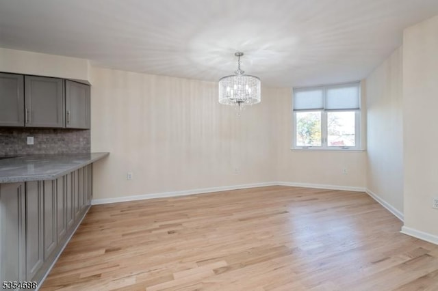 unfurnished dining area featuring baseboards, light wood finished floors, and a chandelier