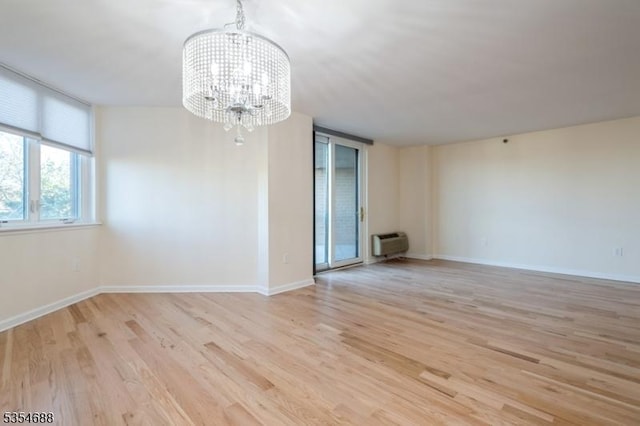 empty room with an AC wall unit, baseboards, an inviting chandelier, and wood finished floors