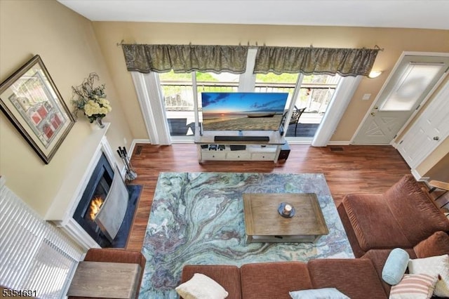 living area featuring baseboards, a warm lit fireplace, and wood finished floors
