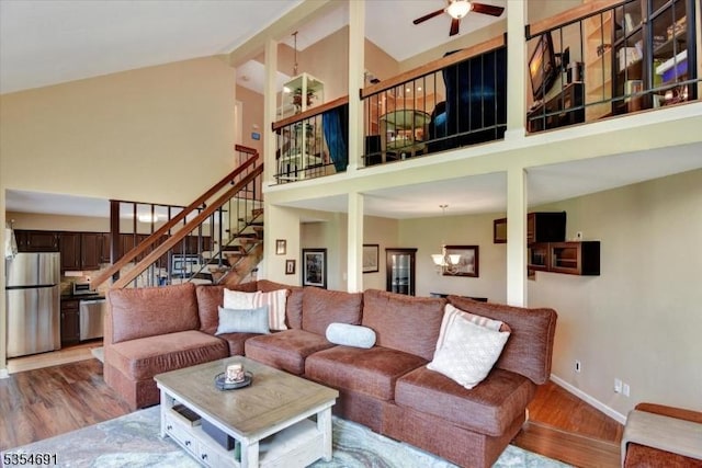 living room with wood finished floors, high vaulted ceiling, baseboards, ceiling fan with notable chandelier, and stairs