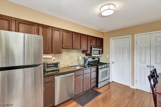 kitchen featuring tasteful backsplash, light wood-type flooring, a toaster, a sink, and stainless steel appliances