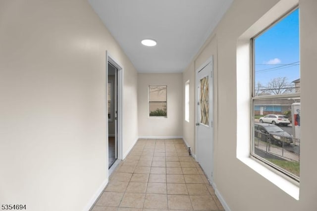 corridor with a wealth of natural light, baseboards, and light tile patterned floors