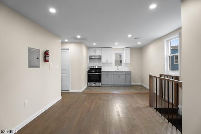 kitchen featuring wood finished floors, a sink, electric panel, baseboards, and gas stove