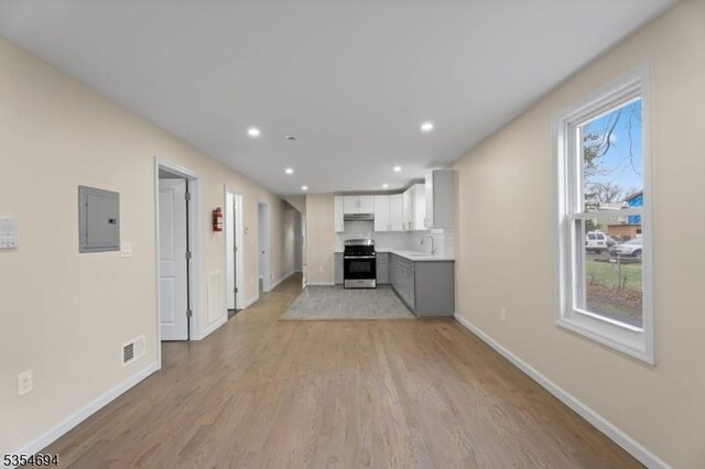 unfurnished living room featuring electric panel, baseboards, light wood-type flooring, and visible vents