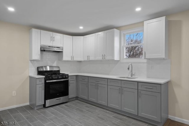 kitchen with under cabinet range hood, stainless steel gas range, a sink, light countertops, and gray cabinets