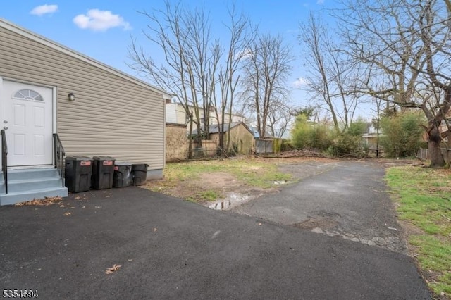 view of yard featuring aphalt driveway, entry steps, and fence