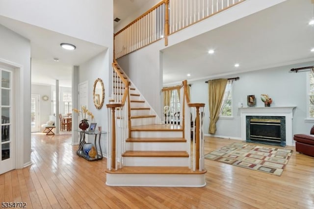 stairway featuring recessed lighting, a fireplace with flush hearth, a high ceiling, and hardwood / wood-style flooring