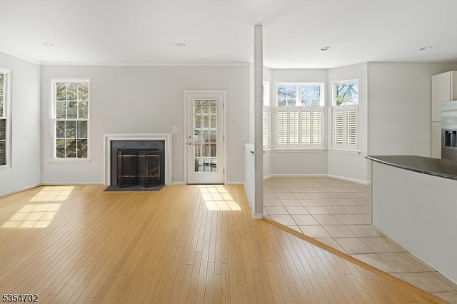 unfurnished living room featuring baseboards, a fireplace with flush hearth, a wealth of natural light, and light wood-style flooring
