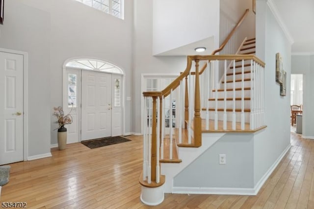 foyer entrance with stairway, baseboards, wood-type flooring, ornamental molding, and a high ceiling