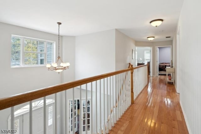 hallway featuring an upstairs landing, light wood finished floors, and a chandelier