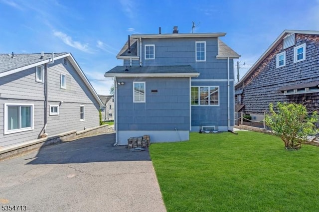 back of house featuring a lawn and roof with shingles