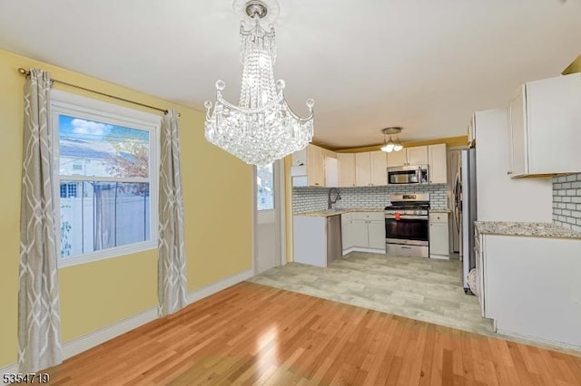 kitchen featuring appliances with stainless steel finishes, a healthy amount of sunlight, an inviting chandelier, and light wood-style floors