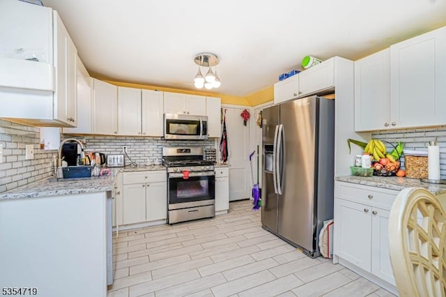 kitchen with white cabinetry, backsplash, light stone countertops, and stainless steel appliances