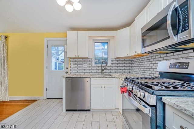 kitchen with backsplash, white cabinetry, a sink, stainless steel appliances, and light wood-style flooring