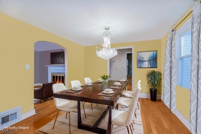 dining area featuring baseboards, visible vents, a glass covered fireplace, and light wood-style floors