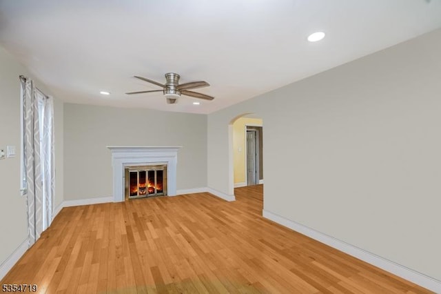 unfurnished living room with a glass covered fireplace, light wood-style floors, baseboards, ceiling fan, and arched walkways