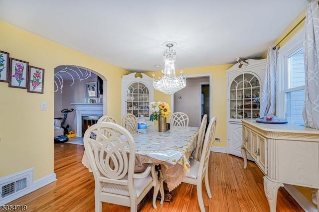 dining space featuring light wood finished floors, a notable chandelier, a warm lit fireplace, and visible vents