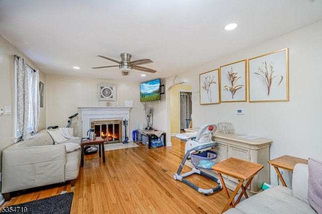 living room featuring a ceiling fan, a fireplace with flush hearth, light wood-style flooring, and recessed lighting