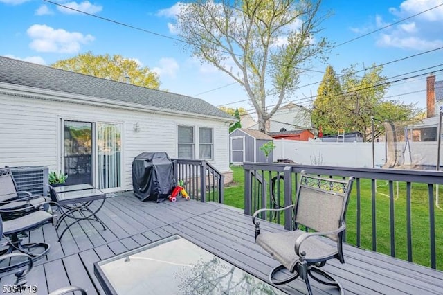 wooden terrace featuring a storage shed, a lawn, fence, an outdoor structure, and a grill