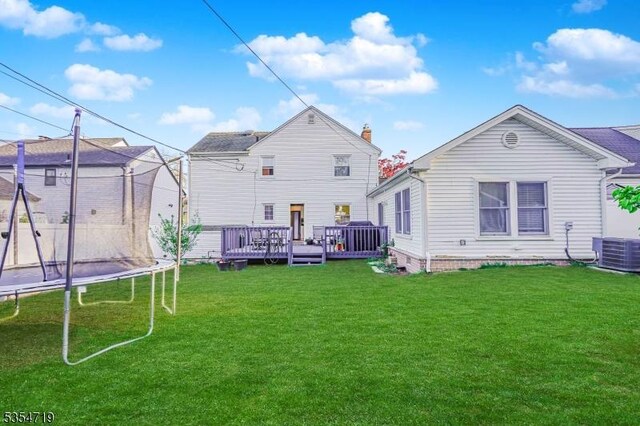 back of property featuring a lawn, a trampoline, cooling unit, and a deck