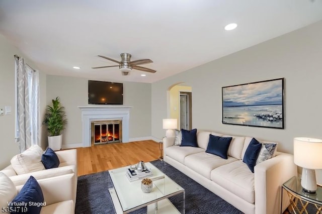 living area featuring a ceiling fan, arched walkways, wood finished floors, a glass covered fireplace, and recessed lighting