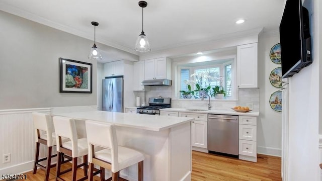 kitchen with crown molding, a sink, a kitchen breakfast bar, stainless steel appliances, and under cabinet range hood
