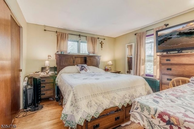 bedroom with light wood-style floors, radiator, and a closet