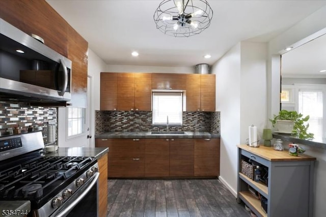 kitchen featuring brown cabinetry, backsplash, appliances with stainless steel finishes, a sink, and dark wood-style floors