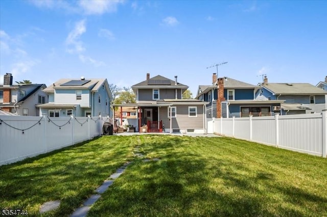 rear view of house featuring a lawn, a residential view, roof mounted solar panels, a fenced backyard, and a patio