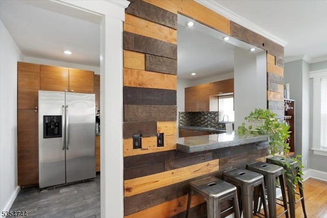 kitchen with decorative backsplash, wood finished floors, stainless steel fridge with ice dispenser, baseboards, and ornamental molding