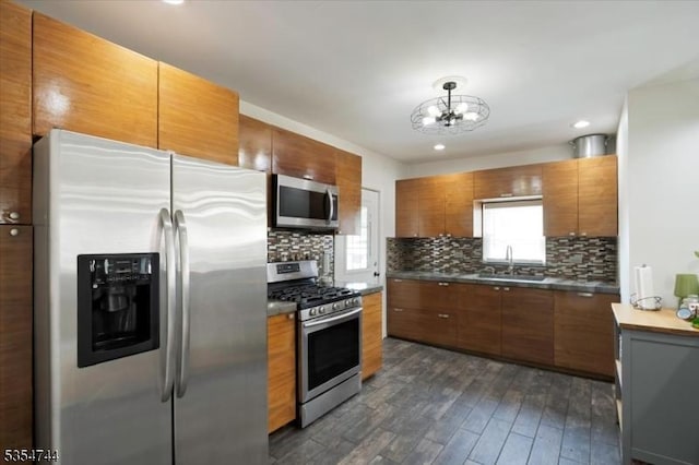 kitchen with a sink, appliances with stainless steel finishes, brown cabinetry, and dark wood-style flooring
