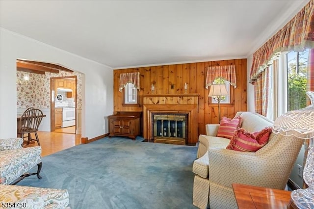 living room featuring crown molding, carpet floors, wood walls, baseboards, and a fireplace with flush hearth