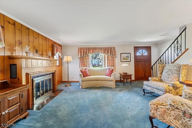 living area featuring a fireplace with flush hearth, crown molding, baseboards, carpet, and stairs