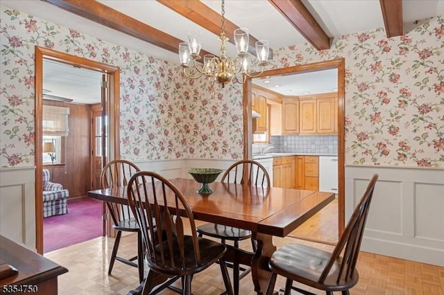 dining space with a wainscoted wall, wallpapered walls, beam ceiling, and a chandelier